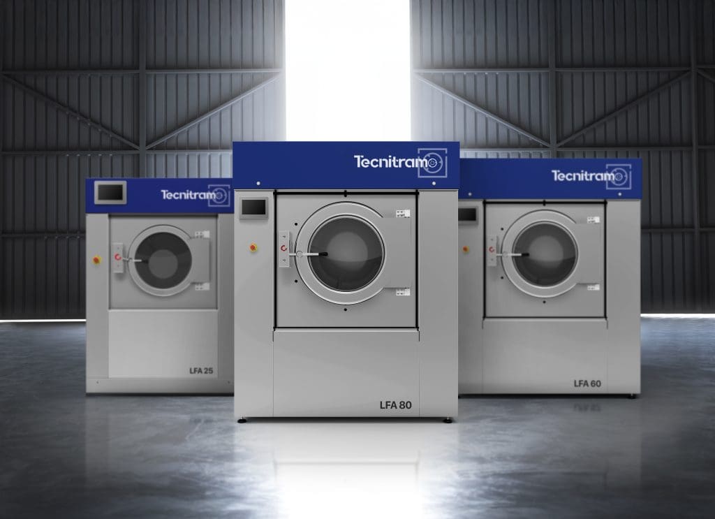 Three industrial washing machines labeled LFA 25, LFA 80, and LFA 60, with a blue "Tecnitramo" sign above each, are arranged in a spacious, well-lit warehouse with large windows in the background.