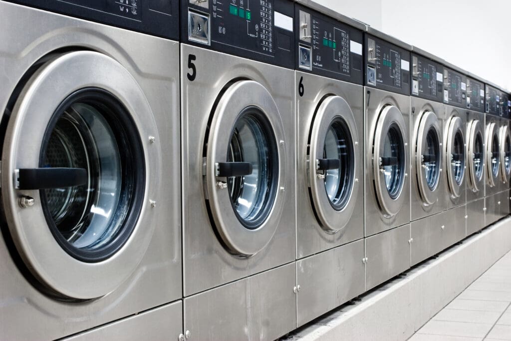 A row of industrial front-loading washing machines numbered 5 to 9 in a laundromat, with stainless steel doors and control panels visible.