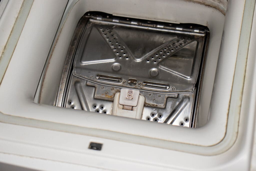 Close-up view of the inside drum of a top-loading washing machine, showing the metallic inner lid and detergent compartment.