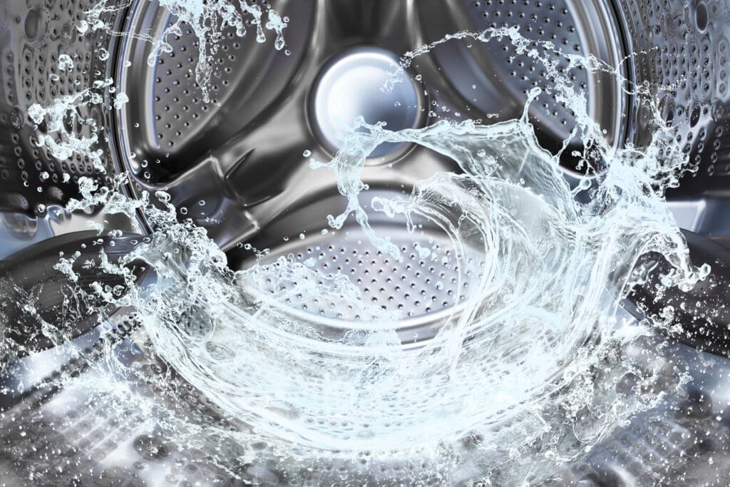 Close-up of water splashing inside a shiny metal washing machine drum, highlighting the motion and cleanliness associated with laundry washing.