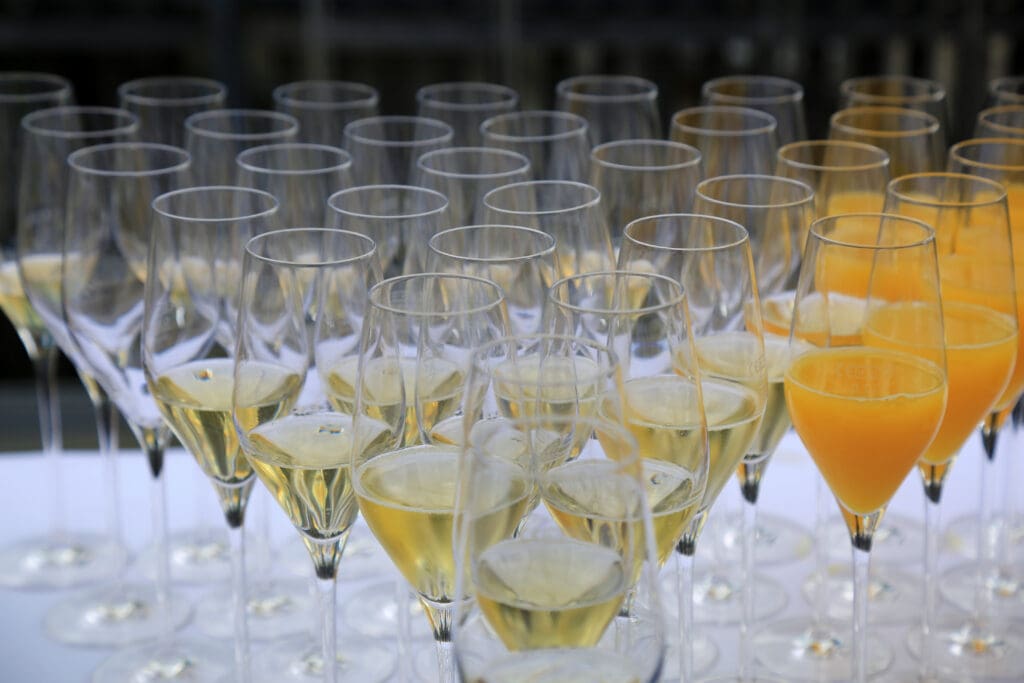 Rows of champagne flutes filled with sparkling white wine and a few filled with orange juice, arranged neatly on a table, ready for a celebration or event.